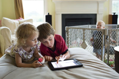 Baby boy looking at siblings using tablet computer while standing in crib