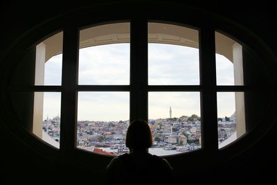 Rear view of silhouette woman looking through window