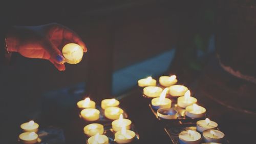 Cropped hand on woman holding lit candle at church