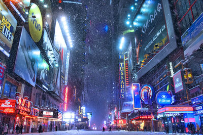 Snow covered street amidst illuminated buildings at night