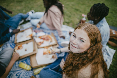 High angle portrait of smiling teenage girl eating pizza with friends at park