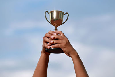 Cropped hands of woman holding trophy against sky
