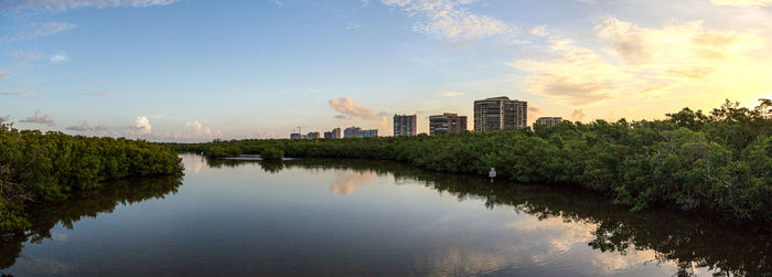 Scenic view of river by buildings against sky during sunset