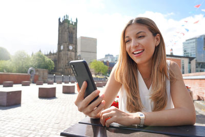 Beautiful young woman is watching videos and photos on her smartphone at the cafe table.