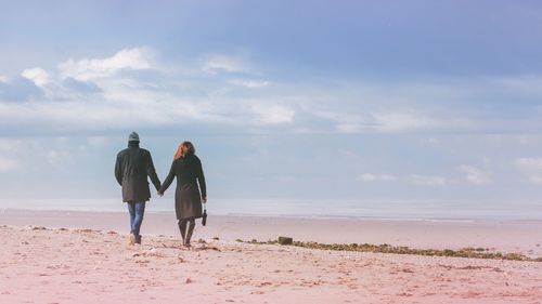 Rear view of people walking on beach against sky