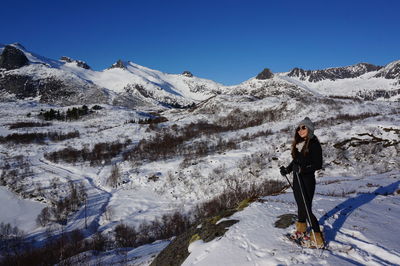 Woman standing on snow covered mountain against clear sky