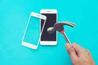 Close-up of hand holding smart phone against blue background