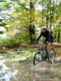 Woman riding bicycle while splashing water in forest