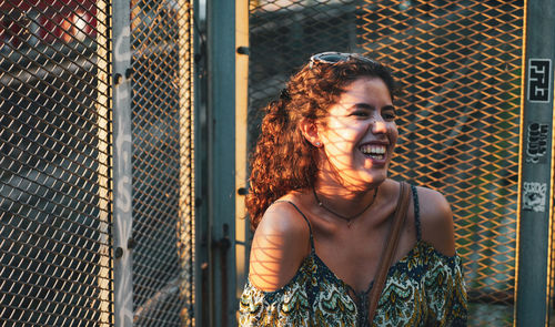 Portrait of smiling young woman standing by fence