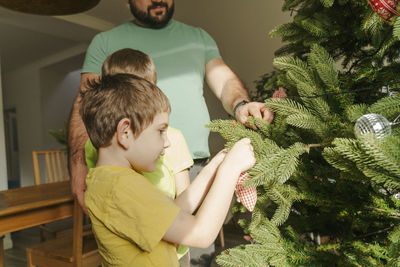 Father assisting sons to decorate christmas tree at home