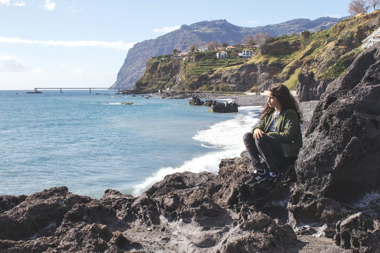 sea, one person, leisure activity, sky, wireless technology, day, water, beauty in nature, horizon over water, outdoors, rock - object, nature, scenics, portable information device, connection, technology, beach, real people, one woman only, adults only, wave, young adult, architecture, adult, only women, people, one young woman only