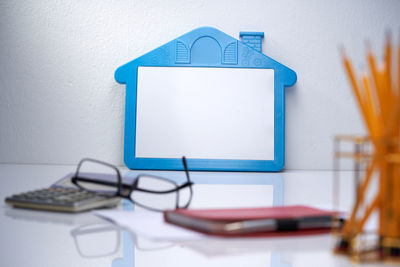 Blank house shaped white board with eyeglasses calculator and diary.