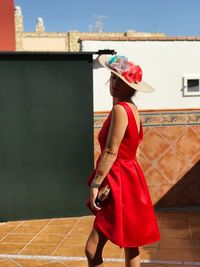 Side view of young woman in dress wearing hat while walking against building during sunny day