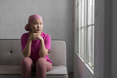 Young woman looking away while sitting on window at home