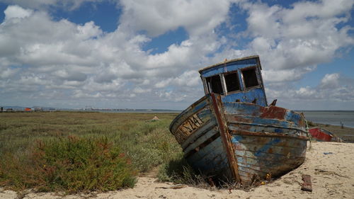Abandoned boat on beach against sky