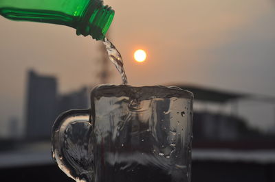 Close-up of water drops on glass against sky during sunset