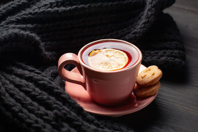 Mug of tea and knitted scarf on black wooden background