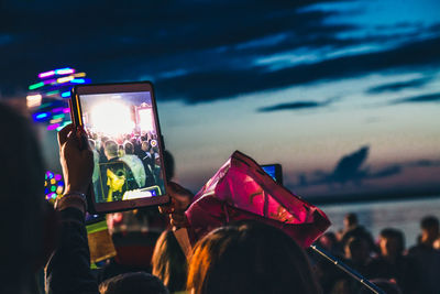 Group of people photographing illuminated smart phone against sky