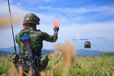 Rear view of man photographing on field against sky