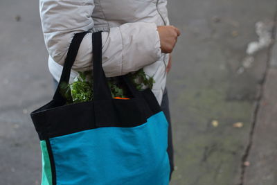 Midsection of woman holding vegetable bag on street