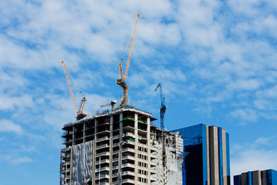 Low angle view of crane by building against sky