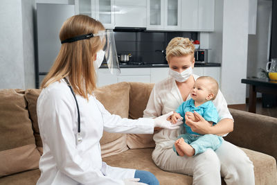 Female doctor examining baby boy at home during pandemic