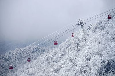 Overhead cable car on snow covered mountains against sky