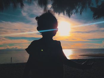 Silhouette boy standing on beach against sky during sunset