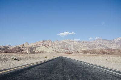 Road amidst desert against clear blue sky