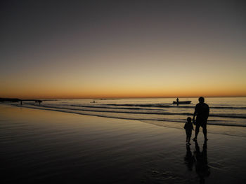 Silhouette of father and son on shore at beach during sunset