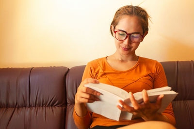 Woman reading book while sitting on sofa at home