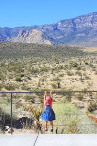 Cute little child observing desert,  hanging on metal bar in front of desert landscape 