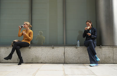 Colleagues eating food while sitting with distance in city