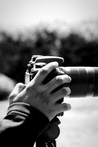 Cropped hand photographing with camera against sky during sunny day