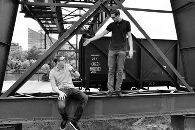 Man pointing towards friend sitting on crane at construction site