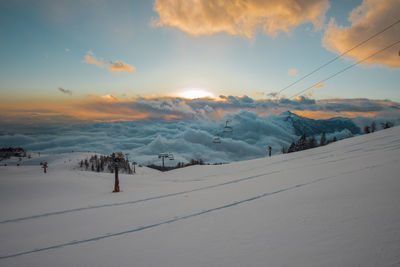 People skiing on snow covered mountain against sky during sunset