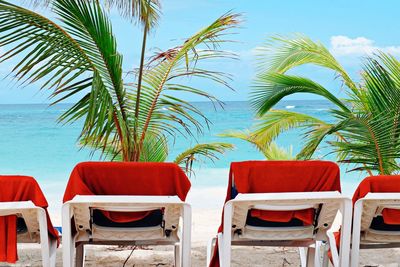 Empty chairs and tables at beach against sky