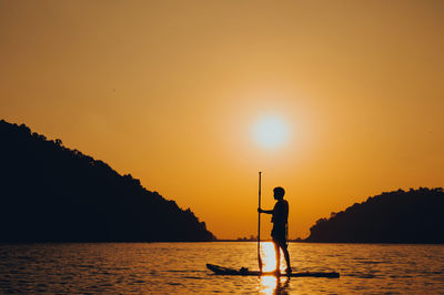 Silhouette man standing in sea against orange sky