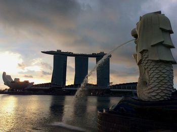 Statue of bridge over river against cloudy sky
