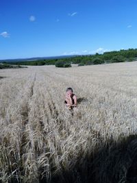 High angle portrait of woman crouching on land against blue sky