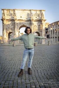 Young smiling man posing for a photo spreading his arms in front of the arch of titus.