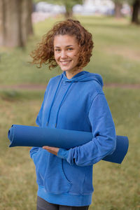 A european woman in a blue hoodie with a blue yoga mat chooses a place to do sports and meditation