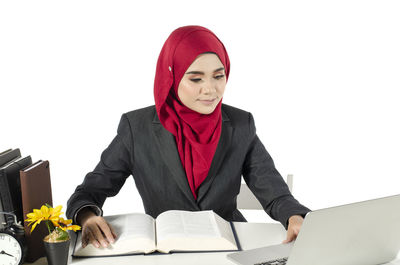 Young woman sitting on table against white background