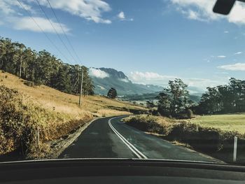 Road amidst trees against sky seen through car windshield