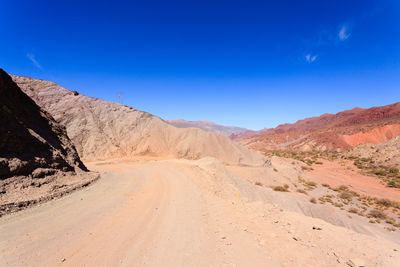 Scenic view of desert road against clear blue sky