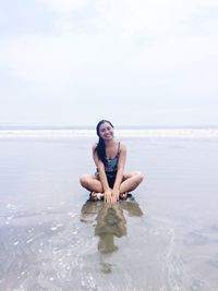 Portrait of smiling woman sitting on wet sand at beach