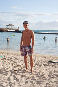 Full length portrait of shirtless man standing on sand at beach