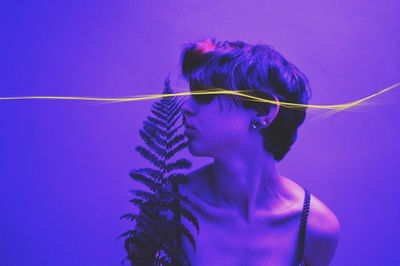 Close-up of woman with leaves and light trail against purple background