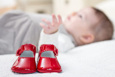 Baby girl lying down by red shoes on bed