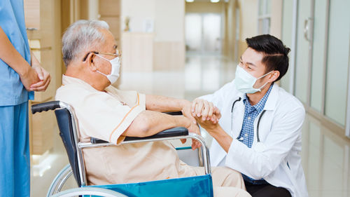 Smiling doctor wearing flu mask consoling patient in hospital